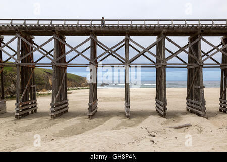 Vista laterale del lungo ponte di legno con vista oceano e giovane attraversando a piedi. Foto Stock