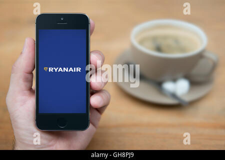 Un uomo guarda al suo iPhone che visualizza il logo di Ryanair, mentre sat con una tazza di caffè (solo uso editoriale). Foto Stock