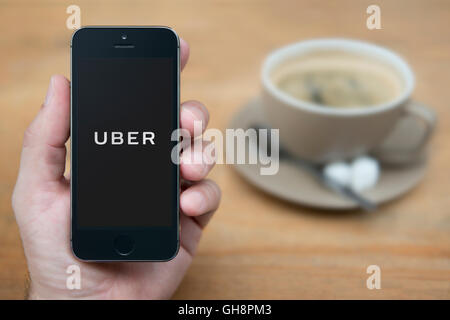 Un uomo guarda al suo iPhone che visualizza il logo Uber, mentre sat con una tazza di caffè (solo uso editoriale). Foto Stock