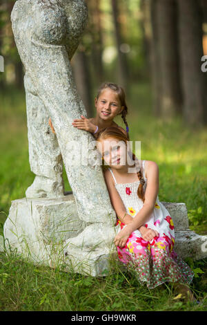 Due graziosi bambine in posa vicino alla statua in un parco. Foto Stock