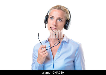 Grave splendido pelo corto donna bionda con cuffia telefonica tenendo occhiali vicino alla bocca mentre guardando verso l'alto su bianco b Foto Stock
