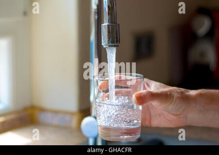 Donna riempire un bicchiere di acqua da un acciaio inossidabile o acciaio al cromo rubinetto, chiudere in su sulla sua mano e il vetro con esecuzione di w Foto Stock