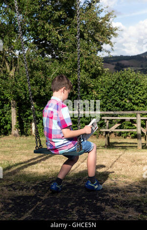 Ragazzo lettura in village park, bambino, park, nero, prati, alberi, amici, relazione, boy, anteriore, ragazza, relax, companionsh Foto Stock