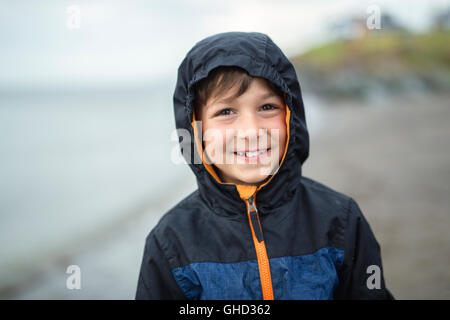 Ragazzo godendo la pioggia e divertirsi al di fuori sulla spiaggia una piovosa grigio Foto Stock