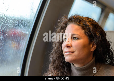 Giovane donna che viaggiano su un treno in un giorno di pioggia seduto guardando fuori le finestre al meteo con un espressione pensieroso Foto Stock