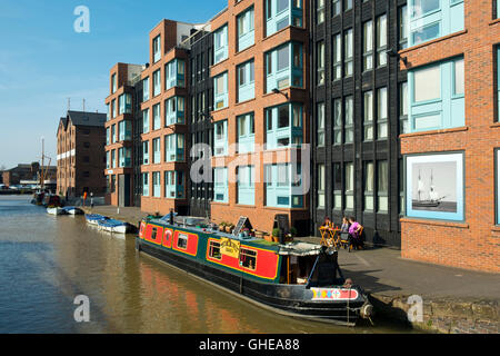 Canal Boat cafe ormeggiato a fianco di costruire nuovi appartamenti e negozi in sole primaverile a Gloucester Docks, Gloucester, Regno Unito Foto Stock