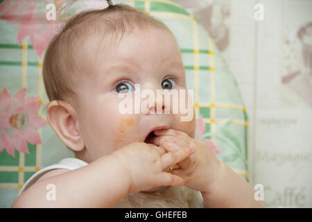 Bambino ragazza si siede in un seggiolone e mangia i cookie Foto Stock