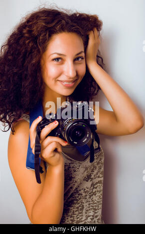 Poco carino ragazza con i capelli ricci tenere la fotocamera, fotografo in un colpo, lo stile di vita di persone concetto Foto Stock