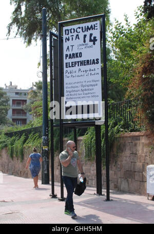 Atene, Grecia. Xiii Sep, 2016. Un uomo cammina davanti ad un cartellone pubblicitario per la mostra in occasione della documenta 14 mentre si parla sul suo smartphone ad Atene, Grecia, 13 settembre 2016. Il documenta 14 ad Atene si apre ufficialmente il 8 aprile 2017 e due mesi più tardi a Kassel in Germania. Foto: Alexia Angelopoulou/dpa/Alamy Live News Foto Stock