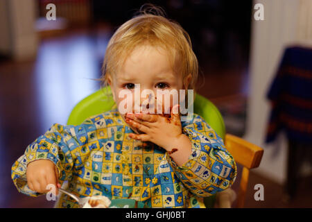 Una bambina di 2 anni di mangiare una torta al cioccolato Foto Stock