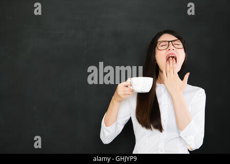 Un buon asian giovane insegnante sente assonnato e di bere il caffè nella scuola Foto Stock