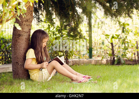 Bambina libro lettura sotto agli alberi Foto Stock