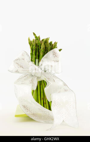 Foto verticale di gambi di asparagi legate con nastro bianco. Ancora in vita con sfondo bianco e copia di spazio. Foto Stock