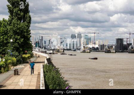 Thames Path accanto al Fiume Tamigi vicino Thames Barrier a sud-est di Londra con Thames Barrier e Canary Wharf torri in background Foto Stock