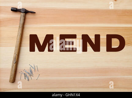 Il martello e il pannello di metallo perni con concetto MEND scritto su uno sfondo di legno Foto Stock