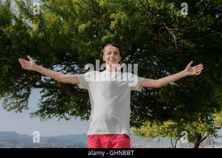 Ritratto di giovane uomo bello aprire in piedi di fronte a un albero Foto Stock