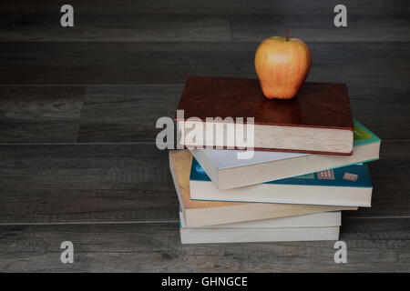 Una pila di libri con un Apple in alto sullo sfondo di legno Foto Stock