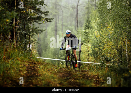 Atleta maschio mountainbiker passeggiate nella foresta durante gare regionali su cross-country bike Foto Stock