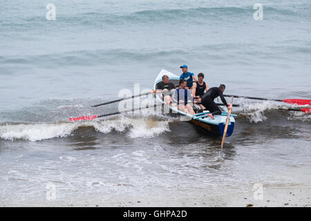 Un team di canottaggio con un gig barca sulla spiaggia di Trevaunance Cove, Sant Agnese, Cornwall, England, Regno Unito Foto Stock