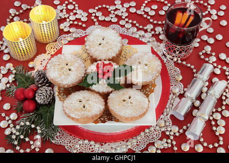 Natale cibo e bevanda ancora la vita con la carne macinata torta torte, agrifoglio, vin brulé, ninnolo decorazioni, cracker di argento e candele. Foto Stock