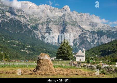 Guardando attraverso il villaggio di Theth con i suoi ciottoli chiesa coperta e le Alpi Albanesi in background, l'Albania settentrionale. Foto Stock