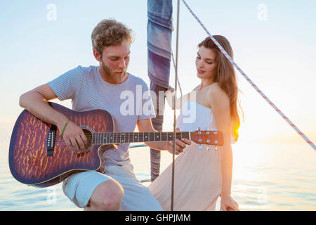 Giovane uomo a suonare la chitarra in barca a vela Foto Stock