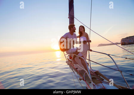 Giovane uomo a suonare la chitarra sulla barca a vela al tramonto Foto Stock