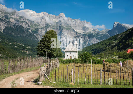 Guardando attraverso il villaggio di Theth con i suoi ciottoli chiesa coperta e le Alpi Albanesi in background, l'Albania settentrionale. Foto Stock