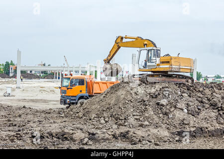 Escavatore giallo è il riempimento di un autocarro con cassone ribaltabile con terreno in corrispondenza del sito di costruzione, il progetto in corso. Foto Stock