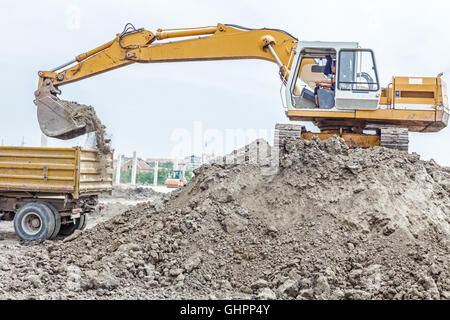 Escavatore giallo è il riempimento di un autocarro con cassone ribaltabile con terreno in corrispondenza del sito di costruzione, il progetto in corso. Foto Stock