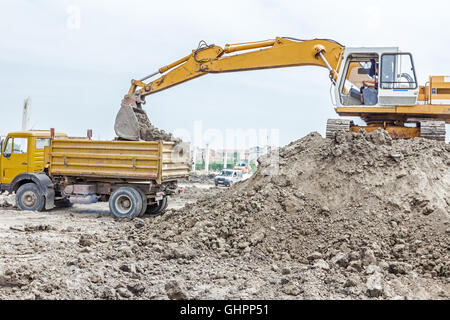 Escavatore giallo è il riempimento di un autocarro con cassone ribaltabile con terreno in corrispondenza del sito di costruzione, il progetto in corso. Foto Stock