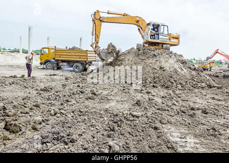 Escavatore giallo è il riempimento di un autocarro con cassone ribaltabile con terreno in corrispondenza del sito di costruzione, il progetto in corso. Foto Stock