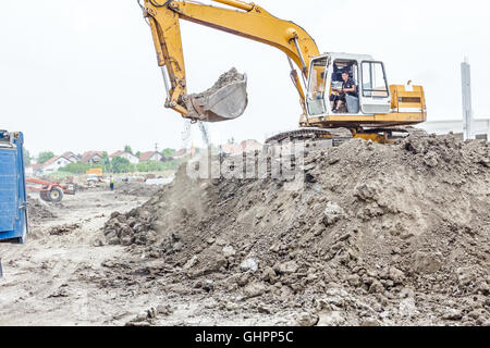 Escavatore giallo è il riempimento di un autocarro con cassone ribaltabile con terreno in corrispondenza del sito di costruzione, il progetto in corso. Foto Stock