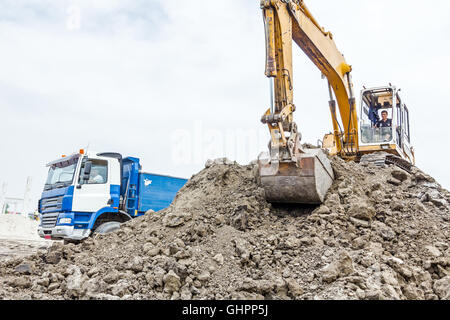 Escavatore giallo è il riempimento di un autocarro con cassone ribaltabile con terreno in corrispondenza del sito di costruzione, il progetto in corso. Foto Stock