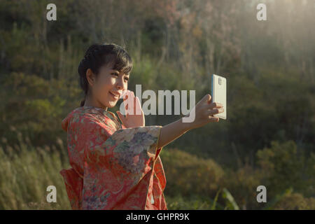 Bel sorriso selfie con lo smartphone in kimono giapponese tradizionale abito in sakura garden. Foto Stock