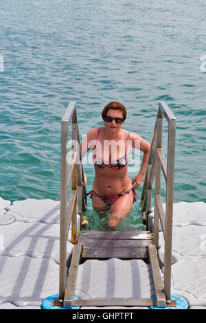 Whete di mezza età donna conciato al nuoto in mare dal ponte galleggiante Foto Stock