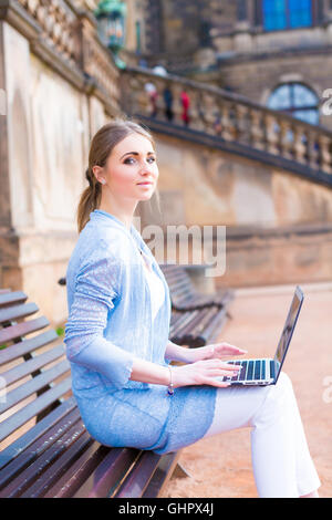 Ragazza lavora su laptop seduta su una panchina nel parco Foto Stock