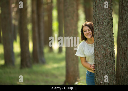 Una ragazza adolescente sorge in corrispondenza di un albero nel parco e sorrisi. Foto Stock