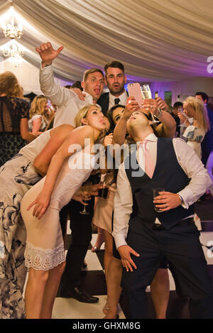 Vista verticale di un gruppo di amici tirando facce buffe pur tenendo un selfie. Foto Stock