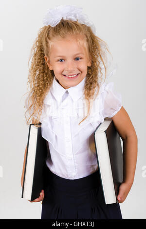 Ritratto di bella sorridente bambina in una scuola uniforme. Essa contiene due grandi libri nelle loro mani Foto Stock