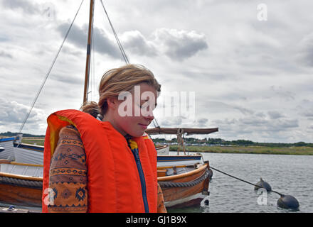 Una giovane donna che indossa un aiuto di galleggiamento attende a bordo la sua barca a vela Foto Stock