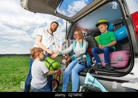 Kid boy aiutando i suoi genitori a loro carico bagagliaio della vettura Foto Stock