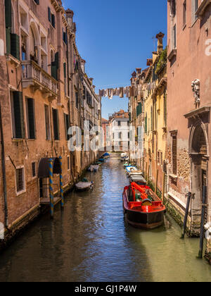 Stretto canale tradizionale con una linea di biancheria appesa attraverso di esso. Barche ormeggiate su entrambi i lati. Venezia, Italia. Foto Stock