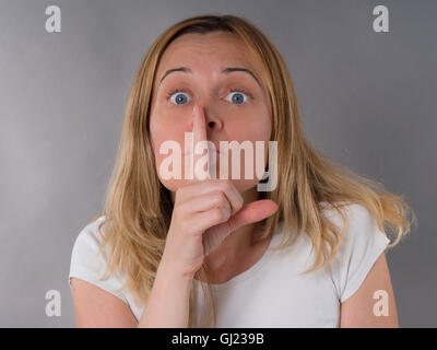 Donna bionda con il dito sulle labbra, silenzio segno Foto Stock