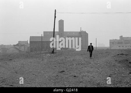 Uomo che cammina attraverso la massa di rifiuti, East End Glasgow 1971 circa Foto Stock