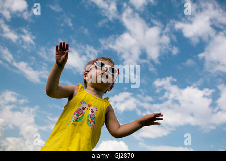 Bambina in un giallo T-shirt con occhiali da sole jumping sullo sfondo del cielo blu. immagine orizzontale Foto Stock