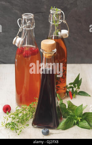 Un assortimento di bottiglie di aceto. Diversi tipi di aceto in varie bottiglie disposte con frutta, erbe e peperoncino Foto Stock