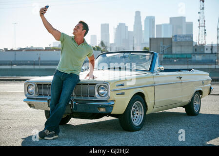 Uomo appoggiato a vettura convertibile tenendo selfie, Los Angeles, California, Stati Uniti d'America Foto Stock