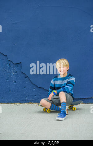 Ritratto di ragazzo seduto su skateboard nella parte anteriore della parete di blu Foto Stock