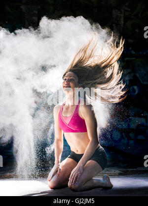 Donna inginocchiata gettare polvere oggetto capelli indietro sorridente Foto Stock